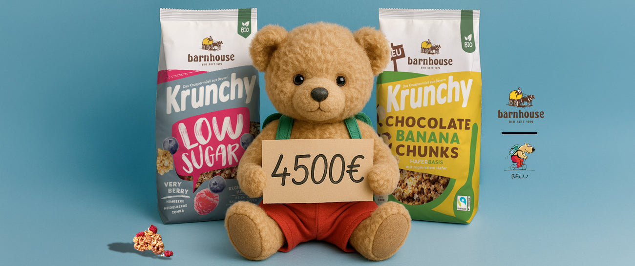 Süßer Teddybär in roter Hose, der ein Schild mit der Aufschrift "4500€" hält. Dahinter stehen zwei Krunchy-Beutel Low Sugar Very Berry (links) und Chocolate Banana Chunks (rechts). Daneben ein Very Berry Cluster sowie die Logos von Barnhouse und BALU.