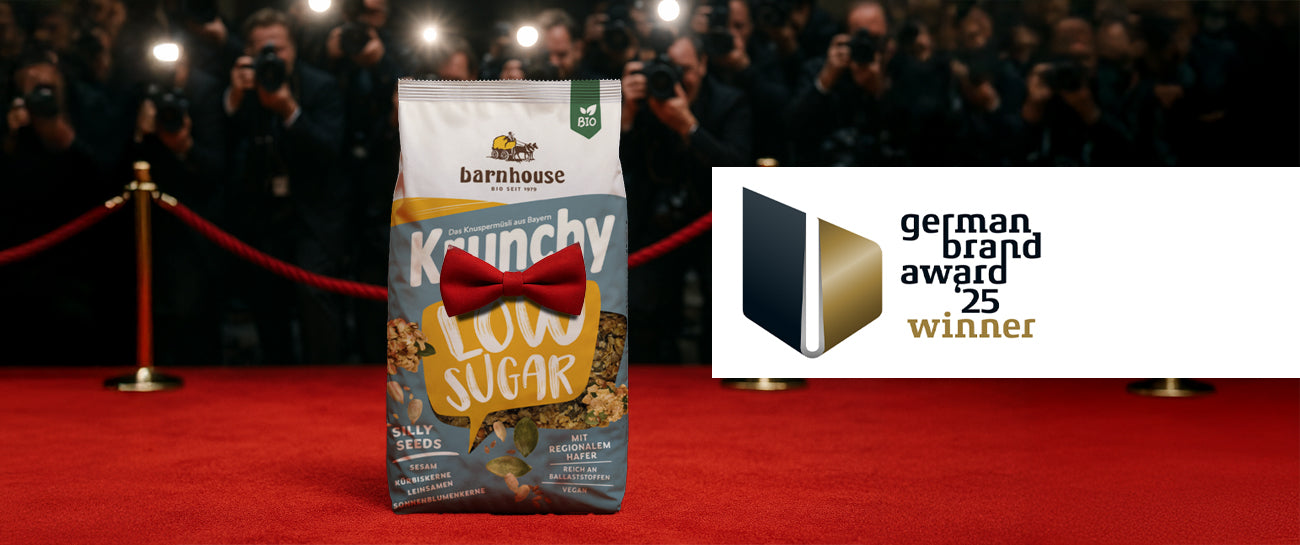 Beutel Krunchy Low Sugar Silly Seeds mit roter Fliege, der auf einem roten Teppich vor lauter Paparazzi steht. Rechts daneben ist das German Brand Award 25 Winner Label abgebildet.