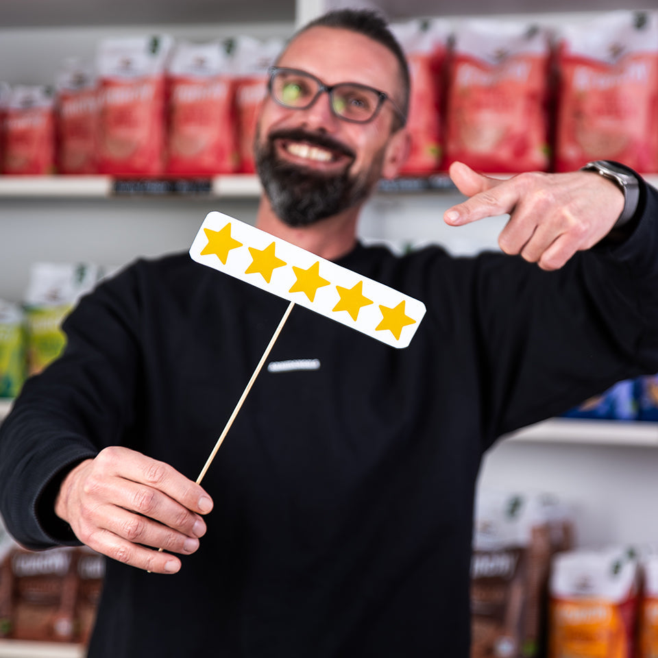 Marketingleiter Andreas hält ein Schild mit 5 Sternen in der Hand und strahlt in die Kamera. Im Hintergrund steht ein Regal mit Krunchy von Bio-Knuspermüsli-Hersteller Barnhouse.