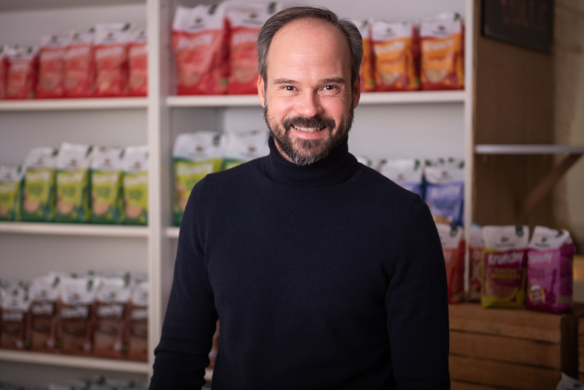 Vertriebsleiter Adrian lächelnd vor einem Regal mit Krunchy von Bio-Knuspermüsli-Hersteller Barnhouse.