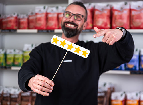 Marketingletiter Andreas steht vor einem Krunchy-Regal und hält ein Schild mit 5 goldenen Bewertungs-Sternen in der rechten Hand. Mit dem linken Zeigefinger zeigt er auf das Schild.