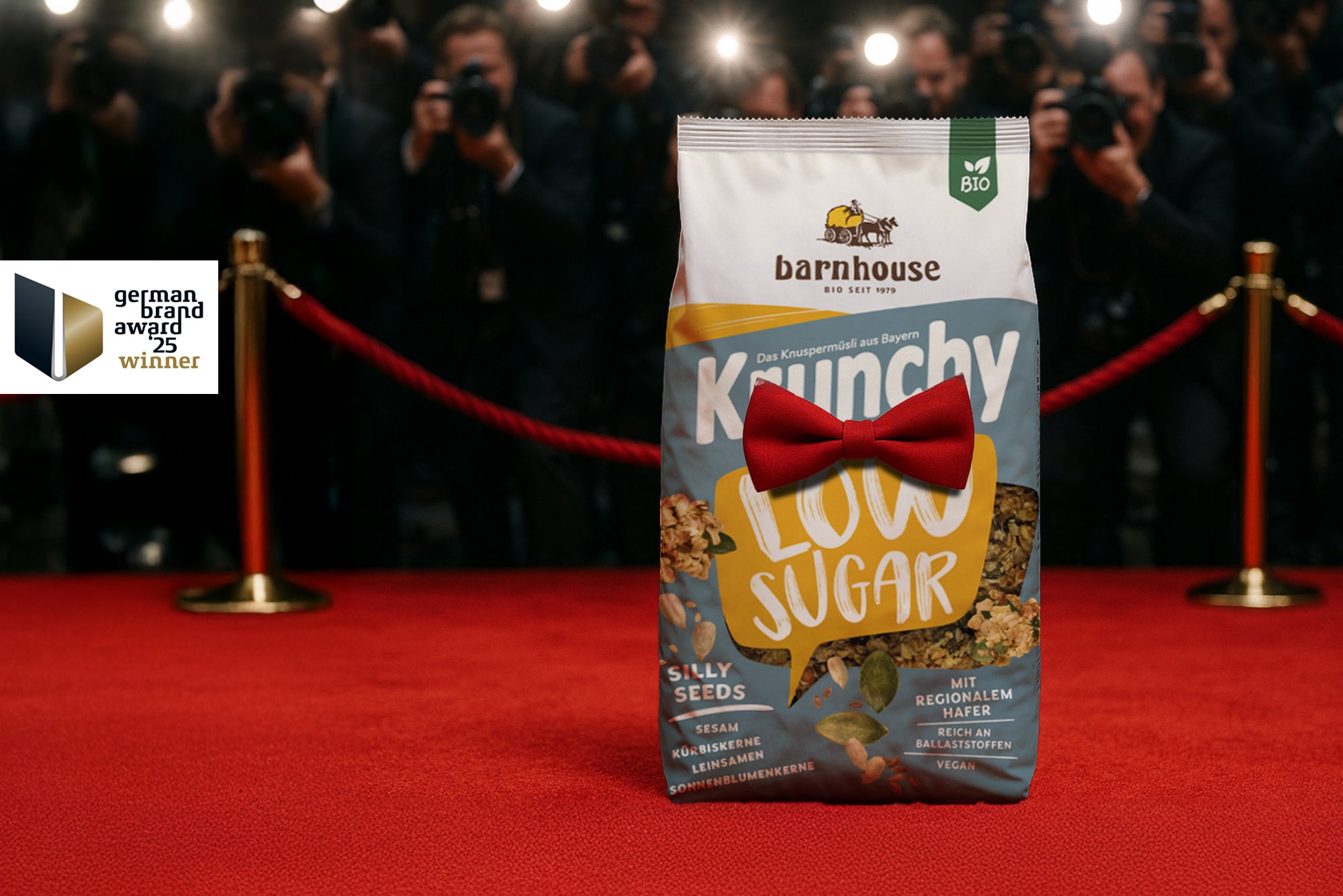 Beutel Krunchy Low Sugar Silly Seeds mit roter Fliege, der auf einem roten Teppich vor lauter Paparazzi steht. Links daneben ist das German Brand Award 25 Winner Label abgebildet.