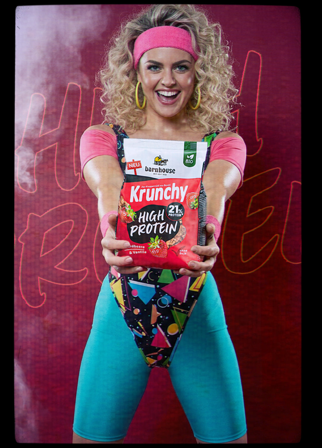 Frau mit bunten Sportklamotten aus den 80er Jahren, die freudestrahlend einen Beutel Krunchy High Protein in ihren Händen hält.