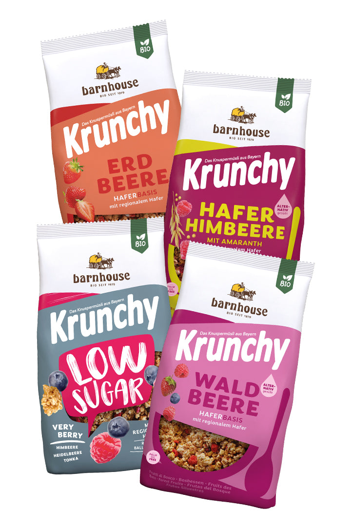 Blick von vorne auf die schräg in 2er Reihe angeordneten Packshots der vier Frucht-Krunchys Erdbeere, Hafer-Himbeere mit Amaranth, Low Sugar Very Berry sowie Waldbeere alternativ gesüßt von Bio-Knuspermüsli-Hersteller Barnhouse.