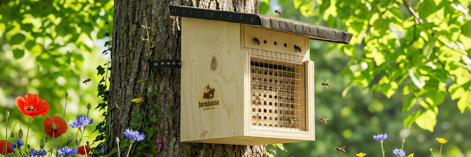BARNHOUSE BEE WILD Nistkasten mit Barnhouse-Logo, der bei Sonnenschein an einem Baum hängt. Außenrum fliegen jede Menge Bienen. Im Hintergrund sind die Äste des Baumes mit grünen Blättern zu sehen und unten ragen verschiedene, bunte Blumen ins Bild.
