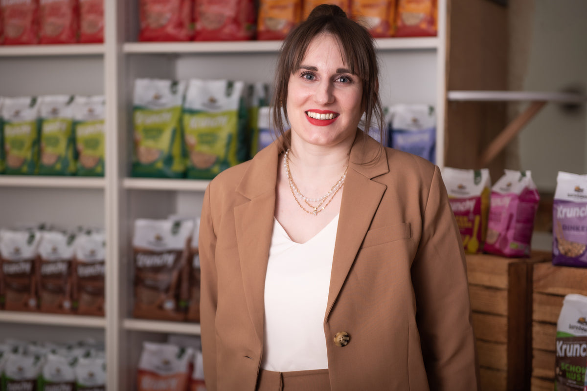 Alicia - Key Account Management
International & Private Label - lächelnd vor einem Regal mit Krunchy von Bio-Knuspermüsli-Hersteller Barnhouse.