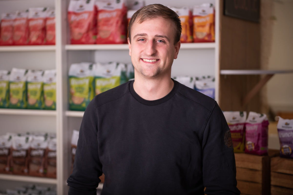 Christian - Leitung Qualität und Produktentwicklung - lächelnd vor einem Regal mit Krunchy von Bio-Knuspermüsli-Hersteller Barnhouse.