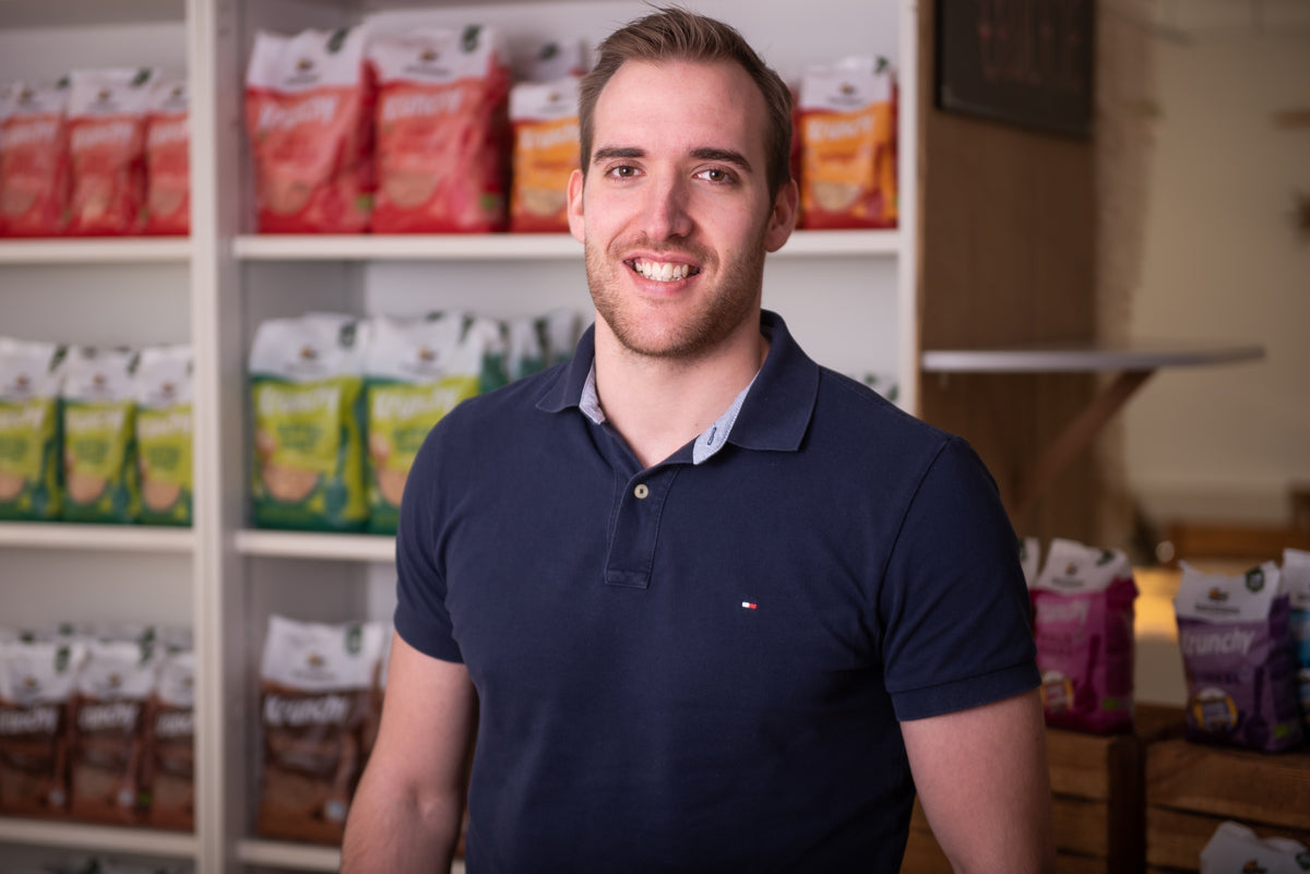 Fabi - Leiter Einkauf und Logistik - lächelnd vor einem Regal mit Krunchy von Bio-Knuspermüsli-Hersteller Barnhouse.