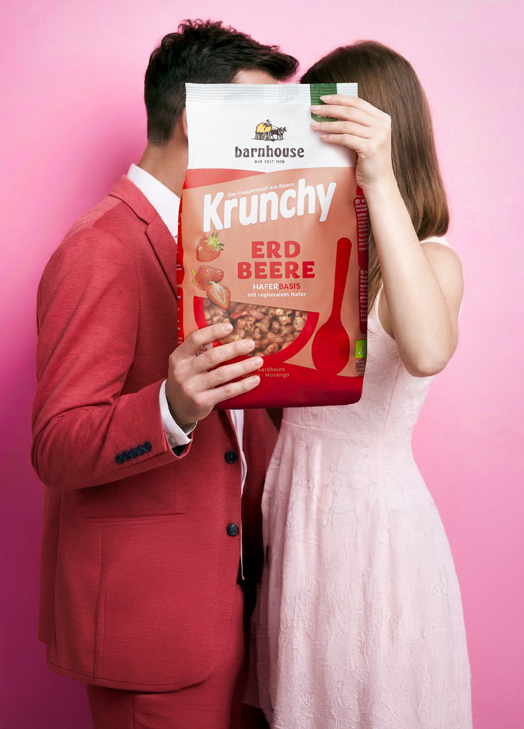 Frau im weißen Kleid & Mann im roten Anzug sind sich sehr nahe. Sieht aus, als würden sie sich küssen. Die Münder werden von XL-Packung Krunchy Erdbeere verdeckt.
