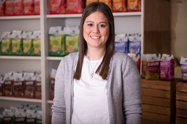Kathi - Key-Account-Management Fachhandel - lächelnd vor einem Regal mit Krunchy von Bio-Knuspermüsli-Hersteller Barnhouse.