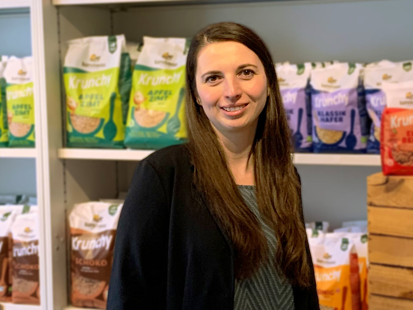 Personalleiterin Kristina Trautmann lächelnd vor einem Regal mit Krunchy von Bio-Knuspermüsli-Hersteller Barnhouse.