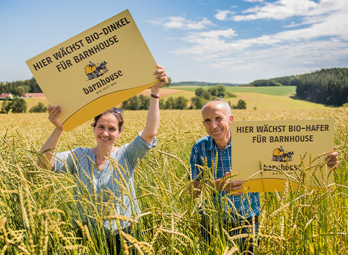 Papa Lex und Tochter Raphaela, Barnhouse Bauern der ersten Stunde, stehen in ihrem Bio-Feld und halten zwei Schilder hoch, dass auf ihrem Feld Bio-Hafer bzw. Bio-Dinkel für Barnhouse wächst.