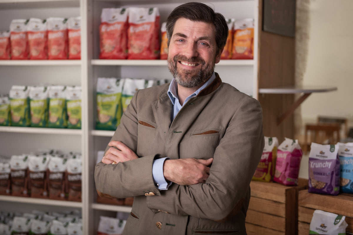 Barnhouse Geschäftsführer Martin Eras lächelnd vor einem Regal mit Krunchy von Bio-Knuspermüsli-Hersteller Barnhouse.