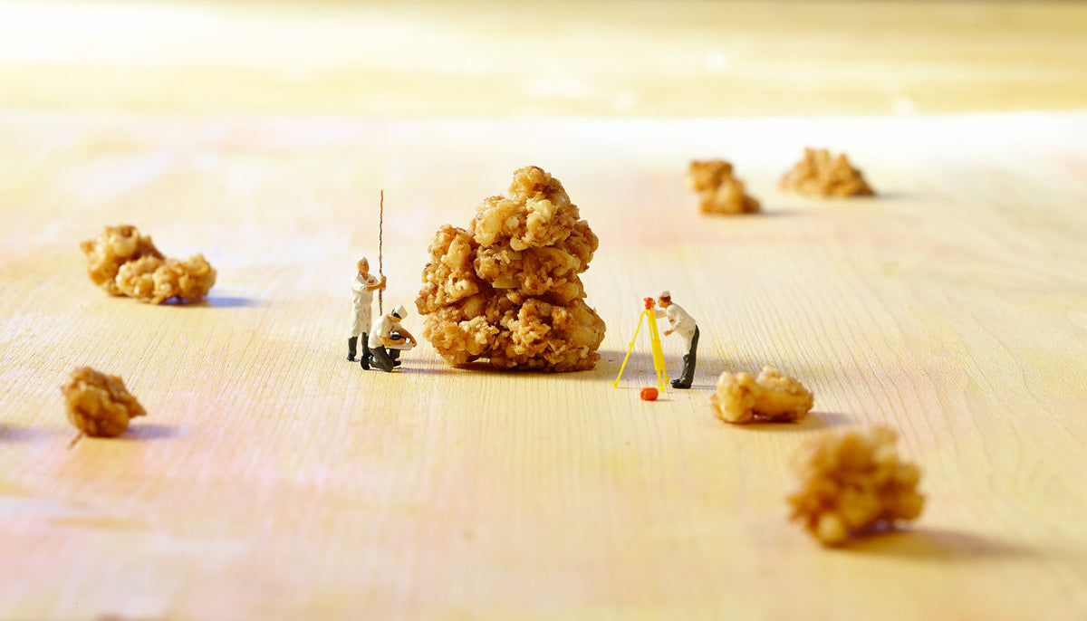 Miniaturbild, bei dem 3 Männchen die Vermessung eines Knuspermüsli-Clusters mit Entfernungsmesser, Meterstab und Notizblock vornehmen. Außenrum liegen noch weitere Cluster.
