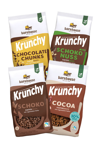 Blick von vorne auf die schräg in 2er Reihe angeordneten Packshots der vier Schoko-Krunchys Schoko-Nuss, Chocolate Chunks, Cocoa weniger Zucker und Schoko von Bio-Knuspermüsli-Hersteller Barnhouse.