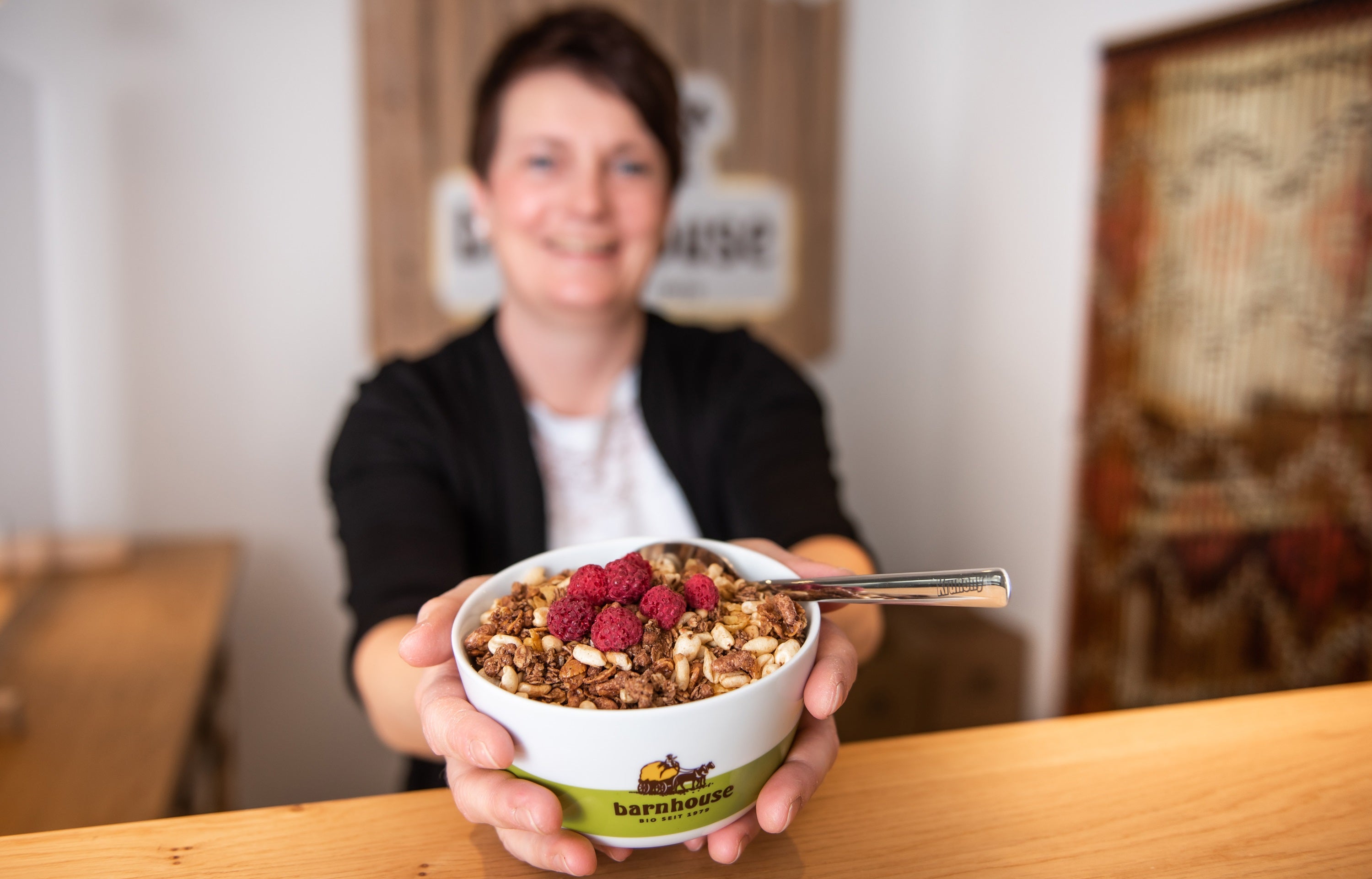 Sabine streckt mit beiden Händen eine Barnhouse-Schüssel mit Krunchy und Himbeeren in die Kamera. 