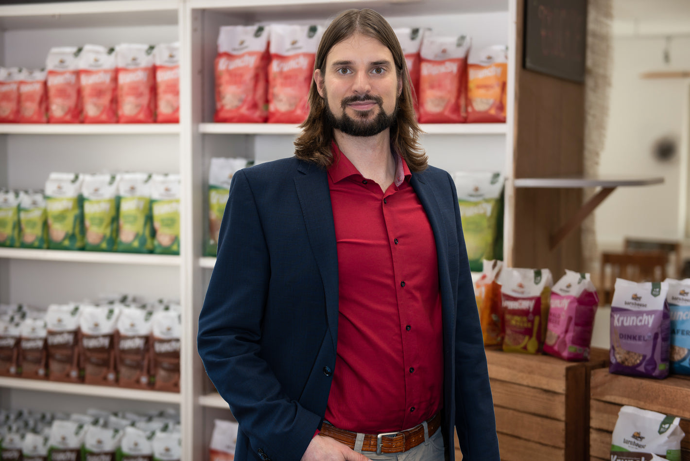 Barnhouse Personalleiter Stephan von Ahnen mit Hemd und Sakko vor einem mit Krunchy befüllten Regal.