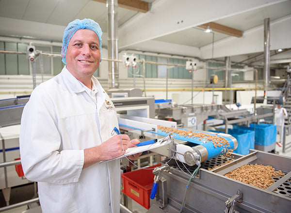 Produktionsleiter Axel steht neben dem Krunchy-Förderband in der Barnhouse Produktion. In der Hand hält er ein Klemmbrett und einen Stift.
