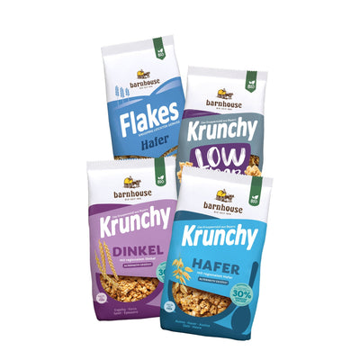 Blick von vorne auf die schräg in 2er Reihe angeordneten Packshots der vier Basis-Produkte Flakes Hafer, Low Sugar Plain Grain, Dinkel 30% weniger Zucker sowie Hafer 30% weniger Zucker von Bio-Knuspermüsli-Hersteller Barnhouse.